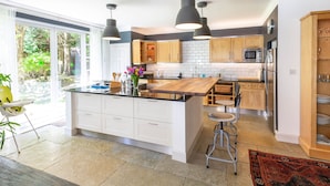 A modern kitchen with a central island, pendant lighting, and a view of the outdoors. - Magnificent Family House with Stunning Private Garden (Drymen)