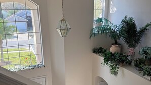 A spacious interior with a large window, a hanging light fixture, and a variety of potted plants. - Villa With Private Pool And Jacuzzi, Ideally Situated for Disney (Clermont)