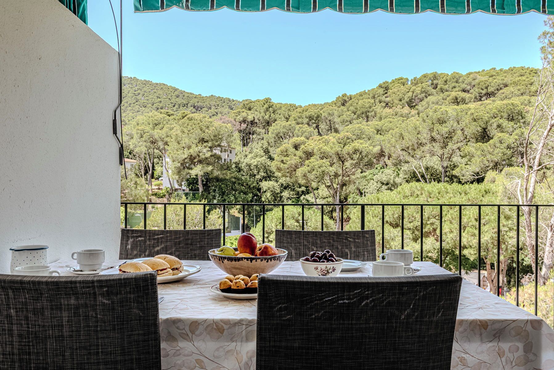 A balcony with a table set for breakfast, overlooking a forested hillside.
