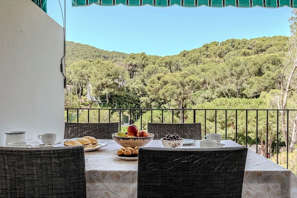 Un balcón con una mesa dispuesta para el desayuno, con vistas a una ladera boscosa.