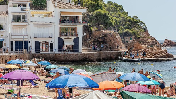 Un bâtiment situé sur la côte, doté de nombreux balcons donnant sur la mer, une plage de sable avec des parasols et des falaises rocheuses.
