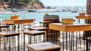 Tables en bois à utiliser en extérieur, avec des pieds en métal, un tonneau en bois et une vue sur la mer avec des bateaux.