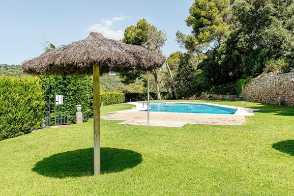 A swimming pool with a thatched umbrella, surrounded by well-maintained grass and trees. - Apartment with swimming pool, terrace, and close to the beach<br>HUTG - 021220 (Tamariu)