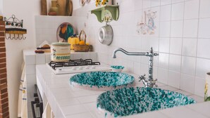 A kitchen with white tiles, a gas stove, two blue and white patterned sinks, a hanging pot rack, and a decorative rooster plate. - Villa Ferradina 4+2, Emma Villas (Ispica (Ragusa))