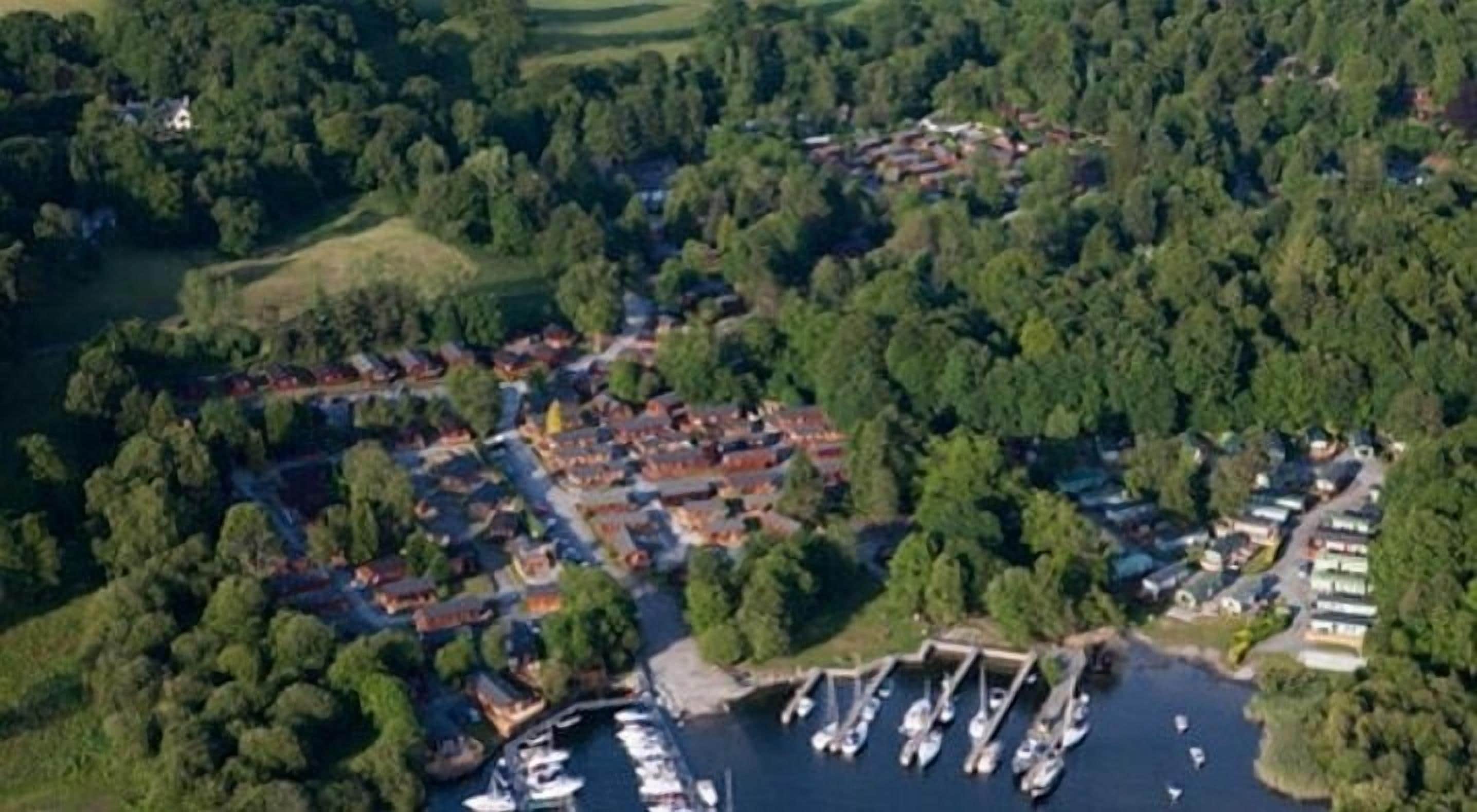 An aerial view of a coastal village with a marina, dense greenery, and residential buildings.