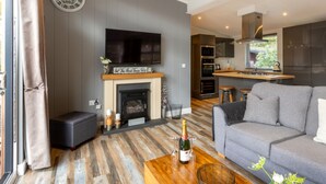 A modern living room with a fireplace, a sofa, and a dining area with a kitchen in the background. - Stunning Lodge set in relaxing surrounding, sleeps 6/8, 3 en-suites, free WIFI (Windermere)