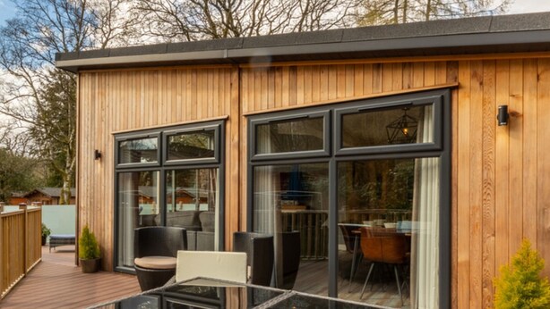 A modern wooden building with large windows and a deck area with outdoor furniture. - Stunning Lodge set in relaxing surrounding, sleeps 6/8, 3 en-suites, free WIFI (Windermere)