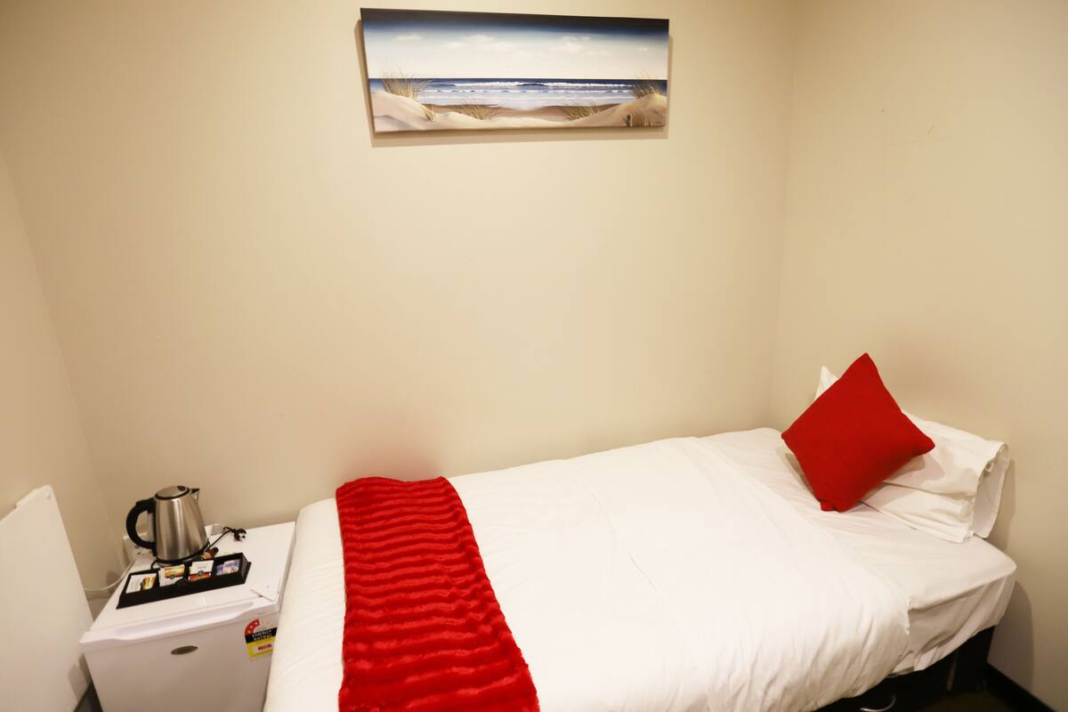 Ein Hotelzimmer mit einem Bett, einer roten Decke, einer Kaffeemaschine und einem Gemälde mit einer Strandansicht.