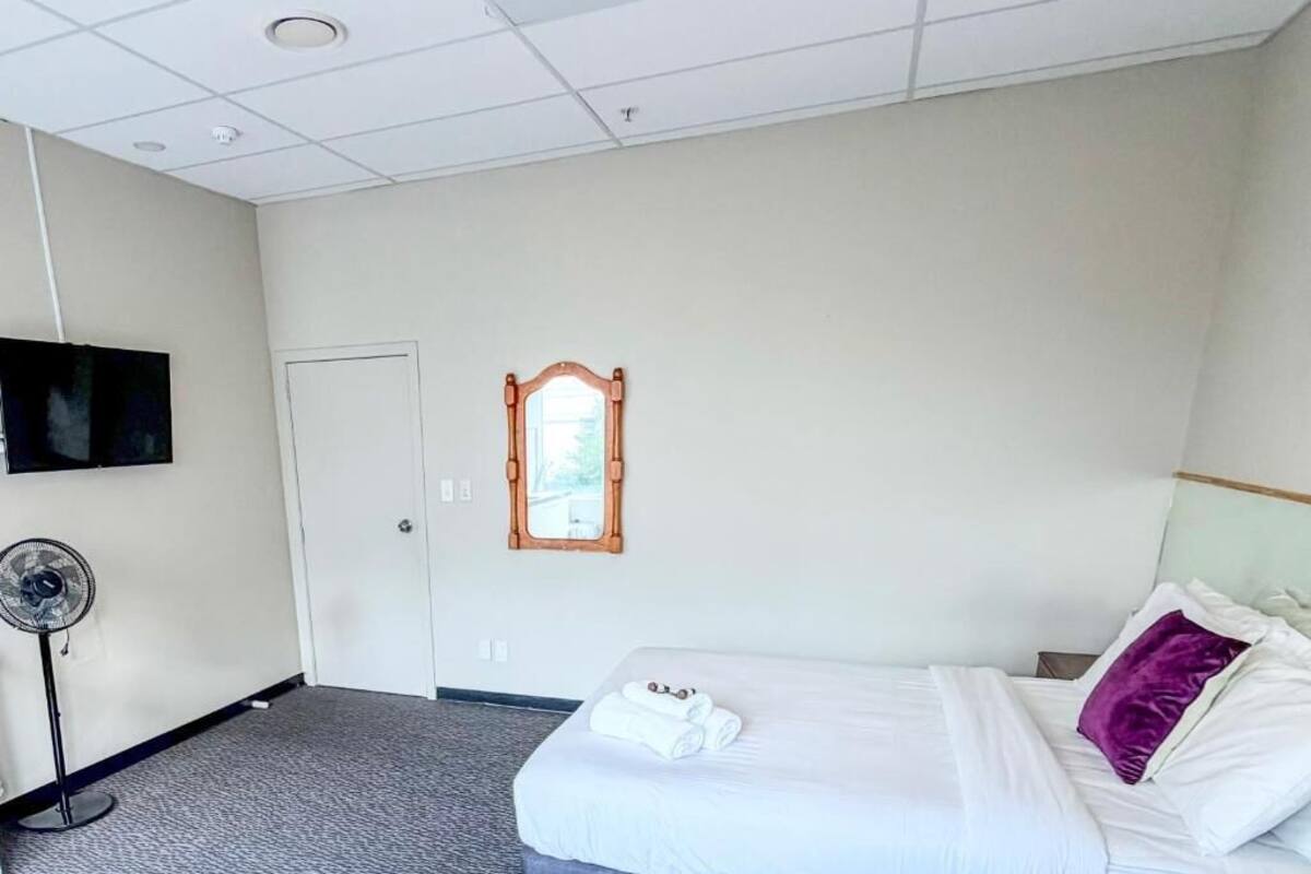 Ein Hotelzimmer mit Bett, Ventilator, Fernseher und einem Fenster mit Holzrahmen.
