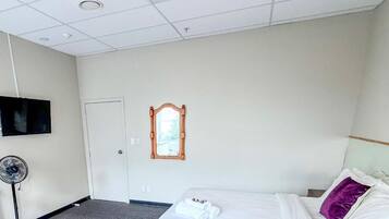 A hotel room with a bed, a fan, a TV, and a window with a wooden frame.