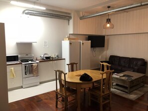 Un espacio habitable compacto con kitchenette, una mesa de comedor y un sofá de cuero negro.