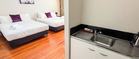 A hotel room with two beds, a small kitchenette, and a painting on the wall.