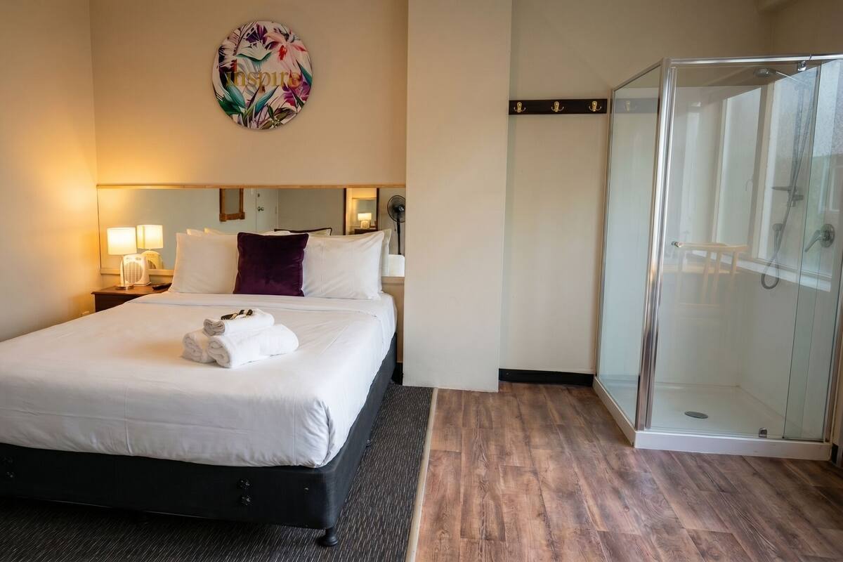 Ein Hotelzimmer mit Bett, Dusche, einem Wandbild und einem Nachttisch mit Lampen.