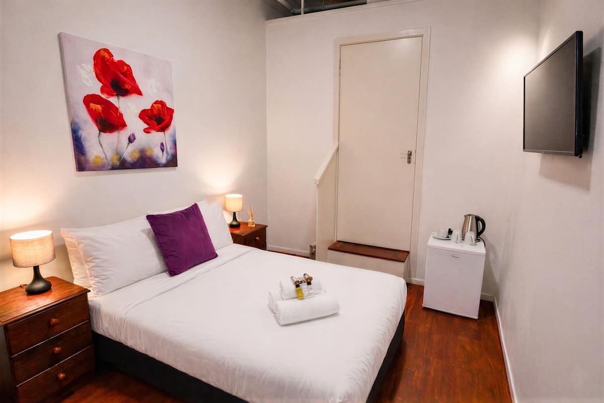 Ein Hotelzimmer mit einem Bett, einem Nachttisch, einem an der Wand montierten Fernseher, einer Tür und einem kleinen weißen Gerät.