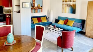 A living room with a blue sofa, red chairs, a wooden coffee table, and a dining area with a red table and chairs.