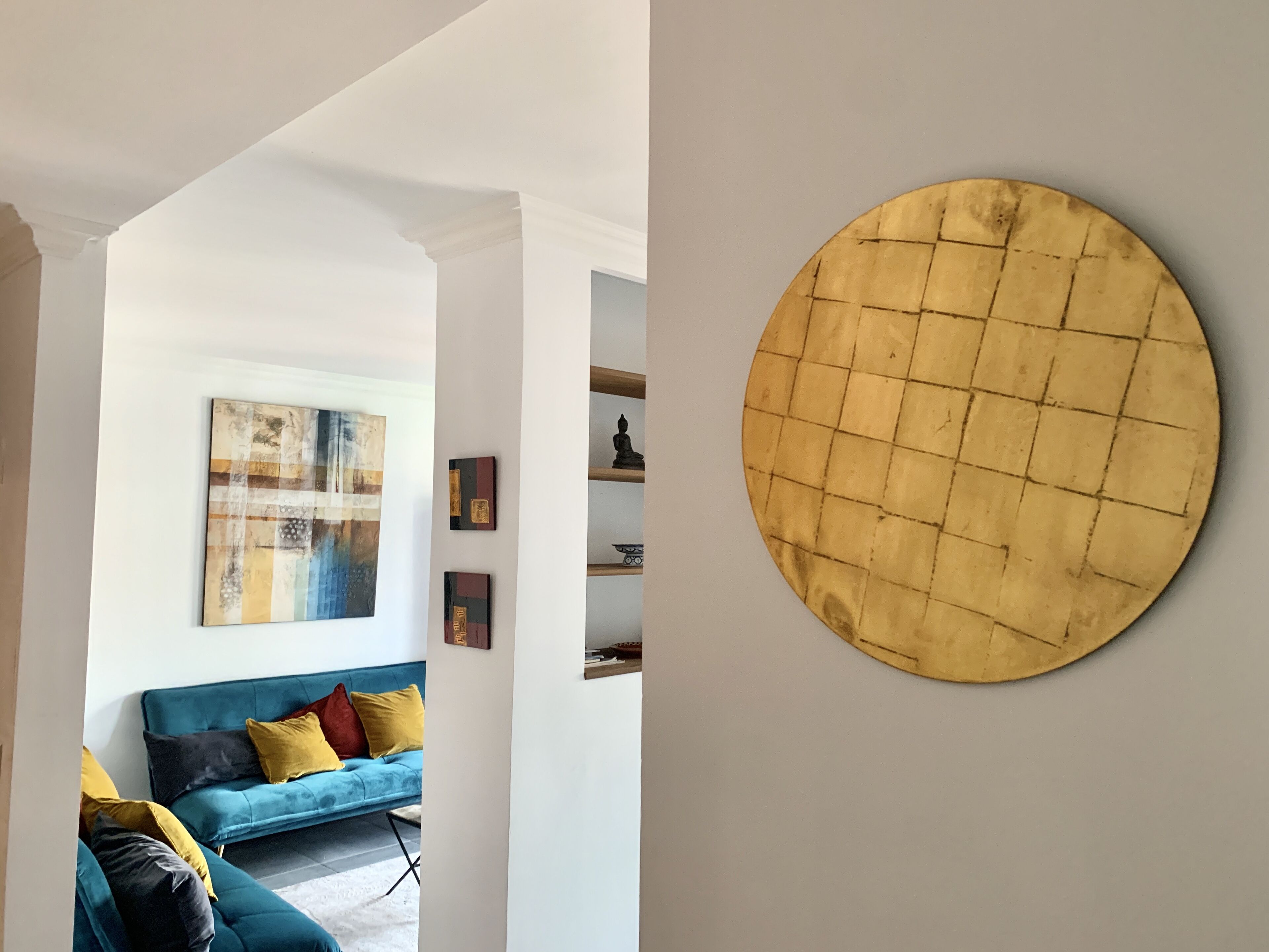 Un salon moderne avec un canapé bleu, des coussins colorés et un grand tableau abstrait accroché au mur.