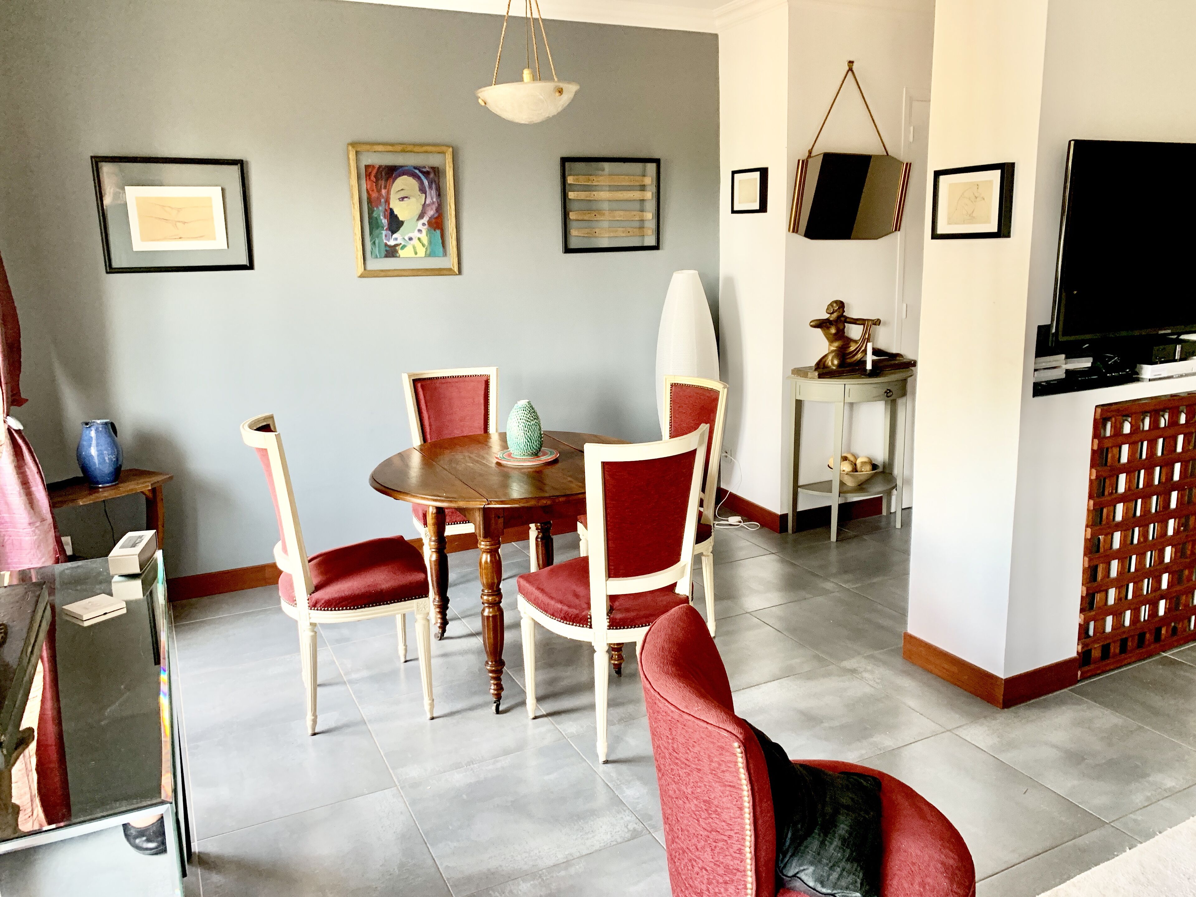 A dining area with a round wooden table, red upholstered chairs, and a hanging light fixture.