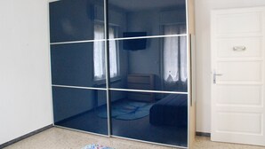 Una stanza con un armadio a vetri scorrevoli, un letto, un comodino e una porta bianca.