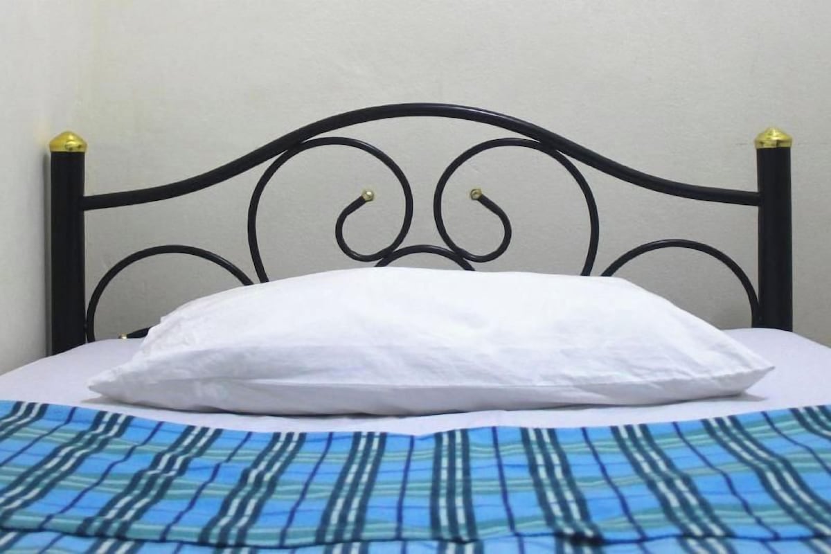 Un lit avec une tête de lit en métal noir, un oreiller blanc et une couvre-lit à rayures bleues et blanches.