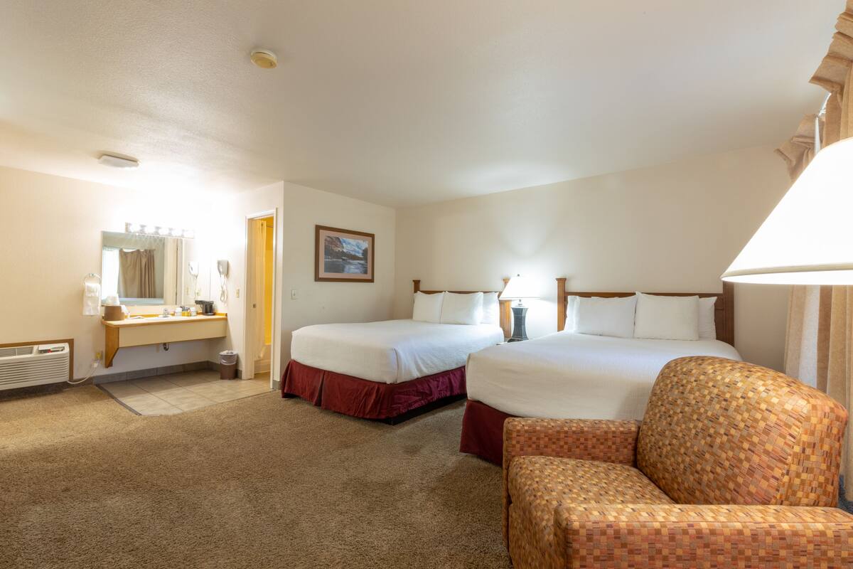 A hotel room with two beds, a sitting area, a vanity with a mirror, and a picture on the wall.