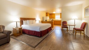 A hotel room with a bed, a desk, a chair, a couch, and a kitchenette. - Clearwater 12 Motel (Kamiah)