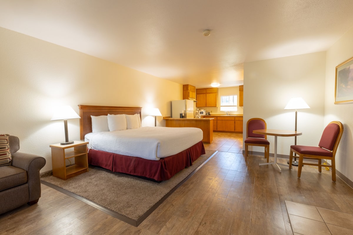 A hotel room with a bed, a desk, a chair, a couch, and a kitchenette.