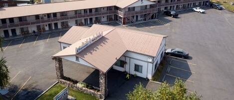 A motel with a central building and two wings, featuring a parking lot and a small garden area.