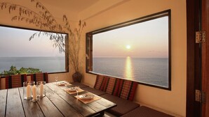 A dining area with a wooden table set for four, large windows overlooking the sea, and a plant in a vase on the wall. - 4 bedroom pool villa (Koh Phangan)