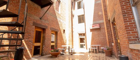 Een binnenplaats met een houten terras, buitenmeubelen en een gebouw van baksteen met een bordje dat een hotellobby aangeeft.