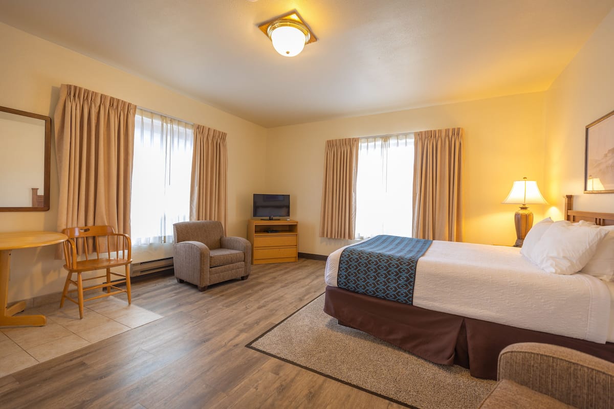 A hotel room with a bed, a desk, a chair, a TV, and a lamp.