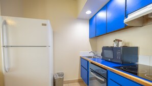 A compact kitchen with a white refrigerator, blue cabinets, a microwave, and a sink. - Helgeson Place Hotel & Suites (Orofino)
