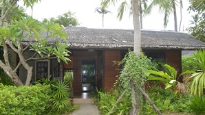 A traditional house with a thatched roof, surrounded by lush greenery and palm trees. - Daetong Resort (Koh Samui)