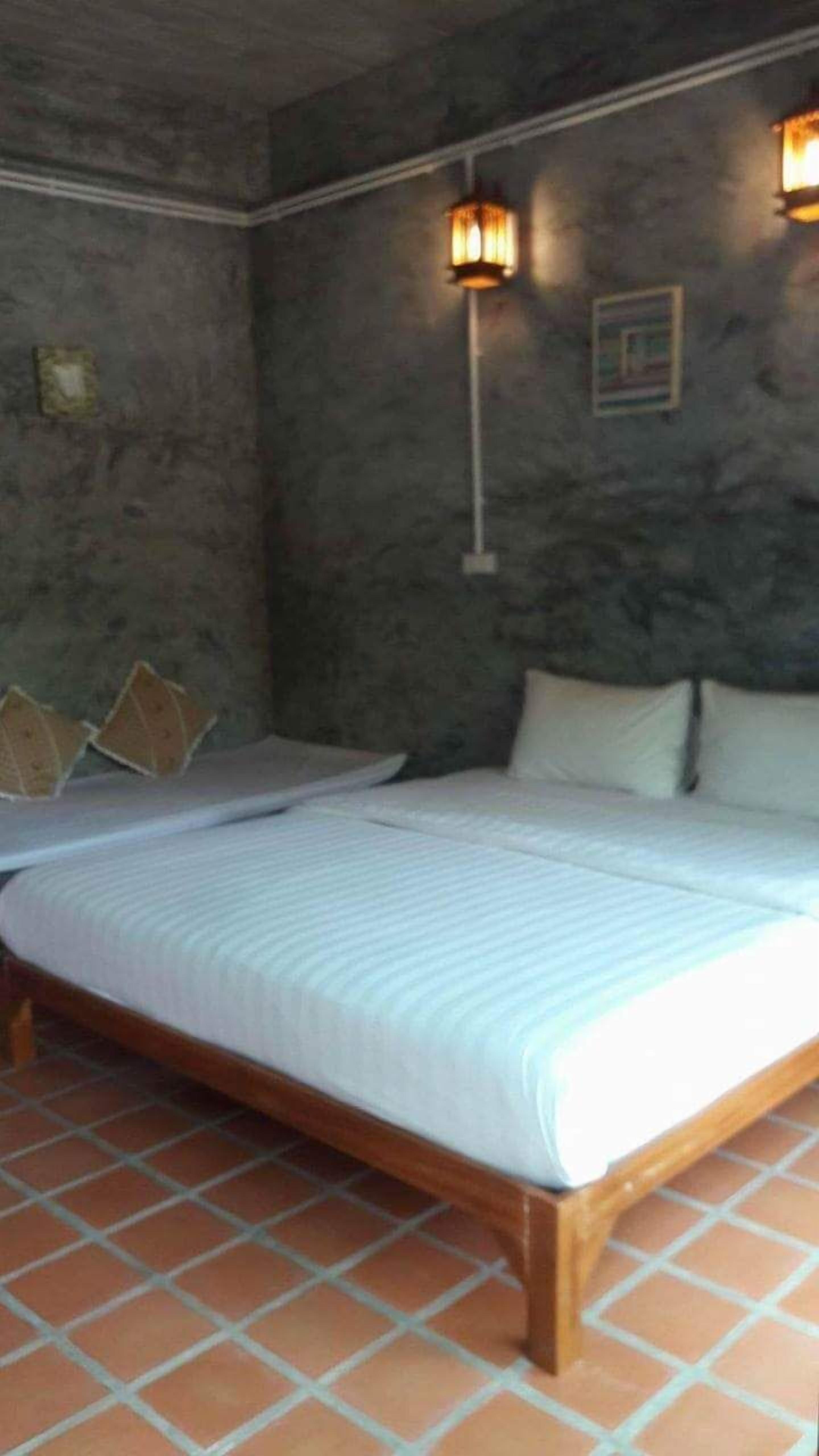 A double bed with a wooden frame and white bedding, two pillows, and a wall-mounted light fixture.