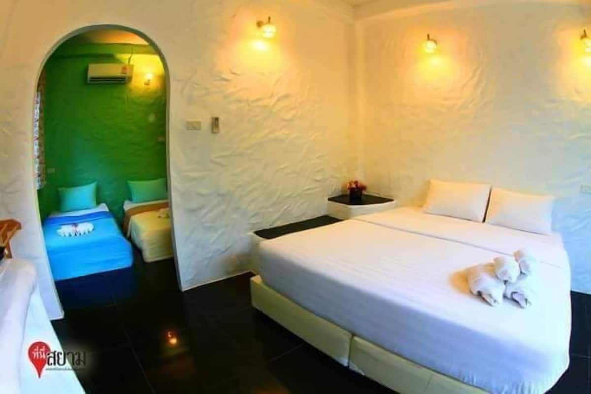 Quarto de hotel com uma cama grande, duas mesas de cabeceira, uma parede verde e uma parede branca com luminárias embutidas.