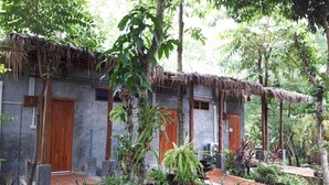 Un edificio rústico con techo de paja, rodeado de abundante vegetación y plantas en macetas.
