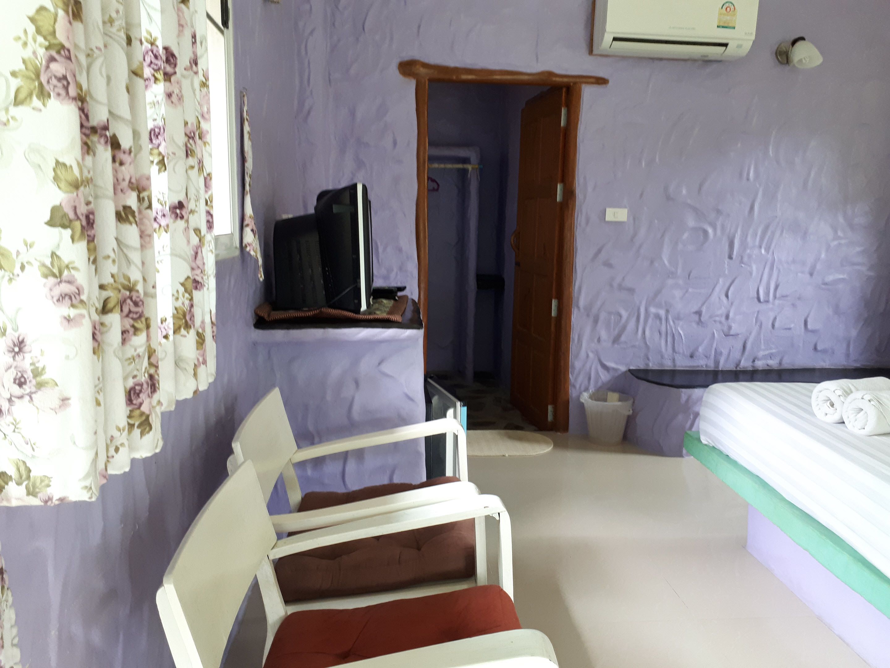 A room with a bed, a chair, a television, and a door leading to another room.