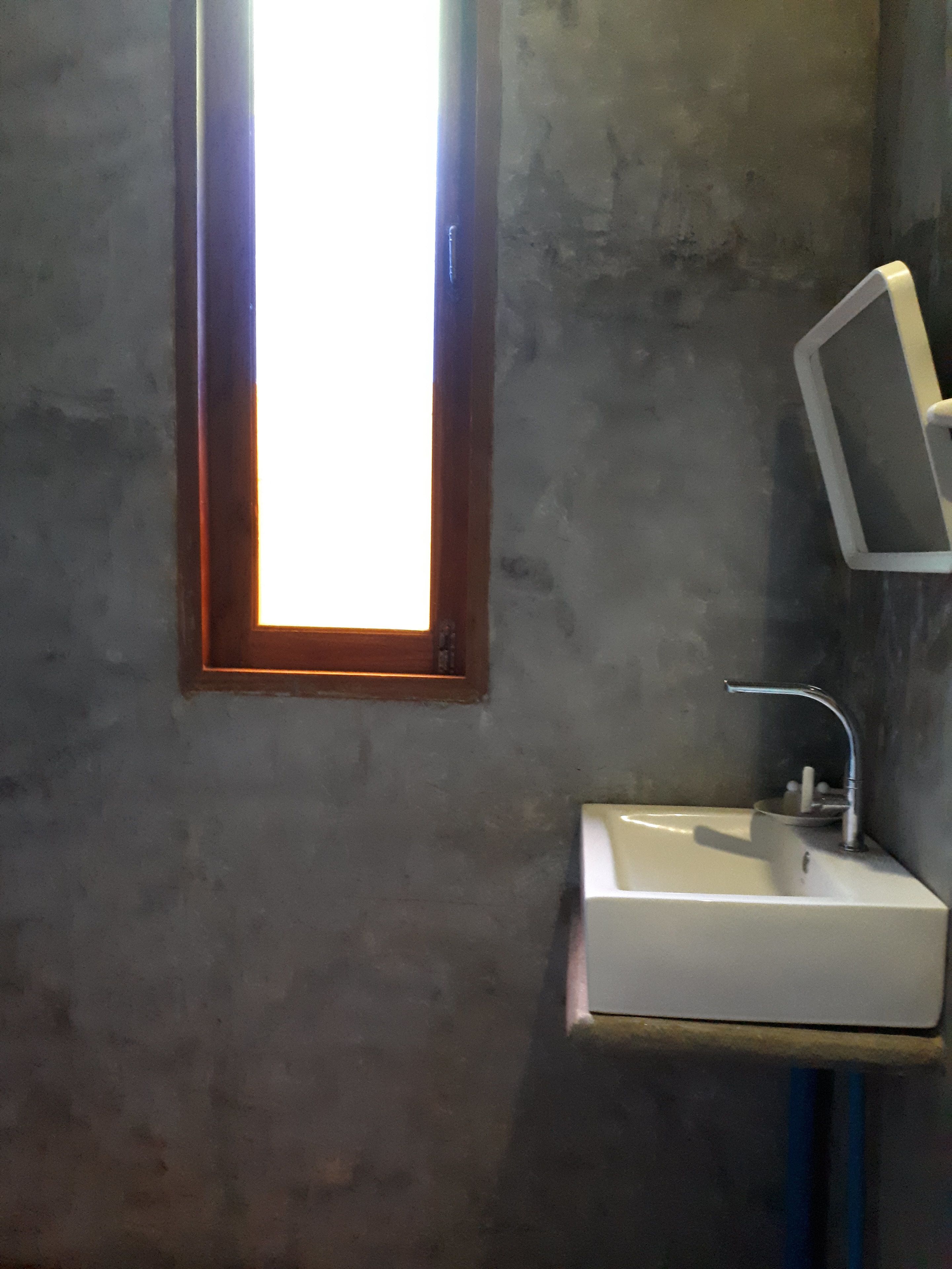 A bathroom with a rectangular window, a white sink, and a mirror mounted on the wall.