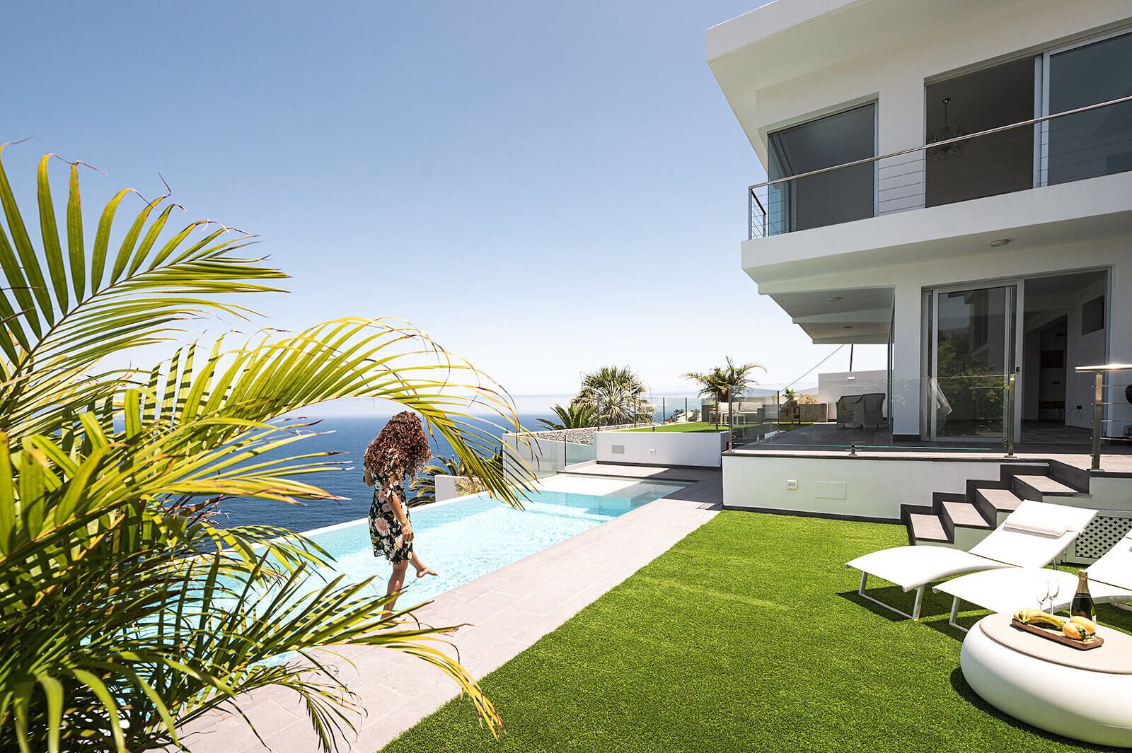 Un espace piscine extérieur moderne offrant une vue dégagée sur l’océan, un bâtiment à deux étages doté de balcons et une pelouse artificielle.