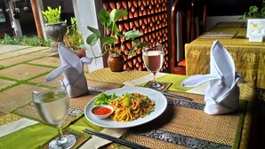 Una mesa dispuesta con un plato de fideos, un vaso de agua y una copa de vino, y una servilleta doblada sobre la mesa.