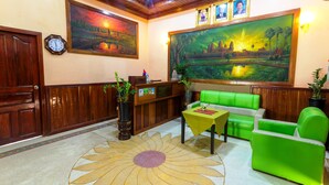 Un vestíbulo con paneles de madera, un mostrador de recepción, asientos verdes, un reloj y dos grandes cuadros con paisajes.