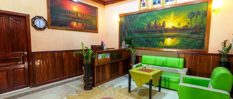 A lobby with wooden paneling, a reception desk, green seating, a clock, and two large landscape paintings.