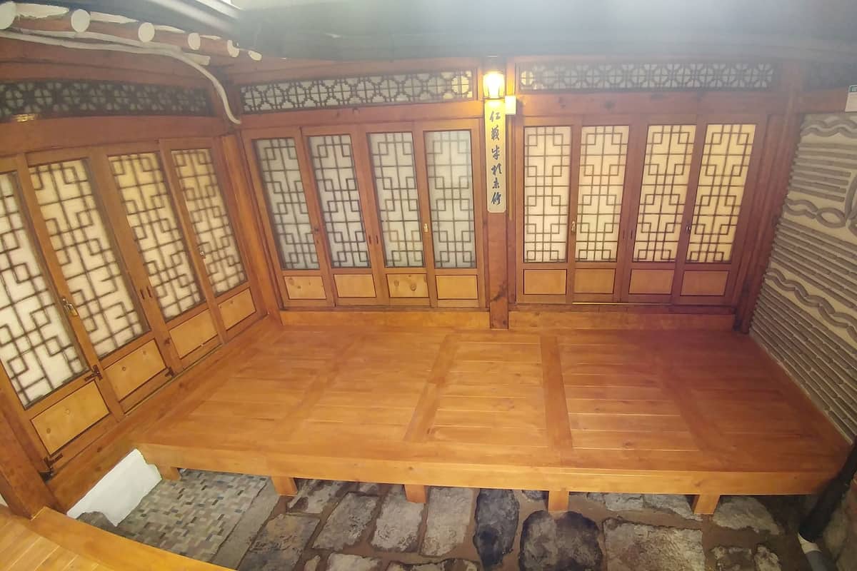 A traditional wooden room with tatami flooring, sliding doors with geometric patterns, and a stone wall.