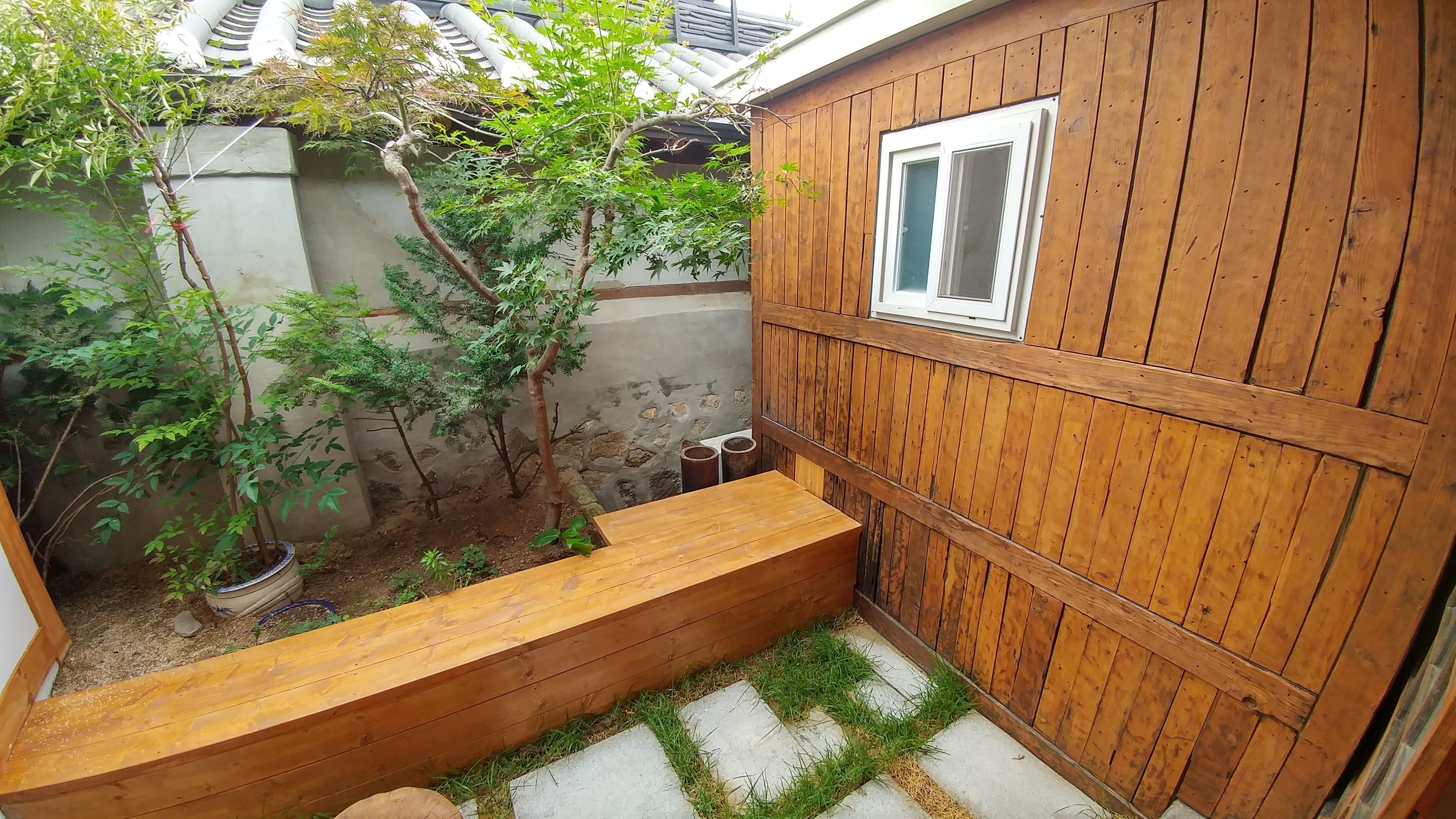 A wooden deck with a built-in bench, a small window, and a potted plant.