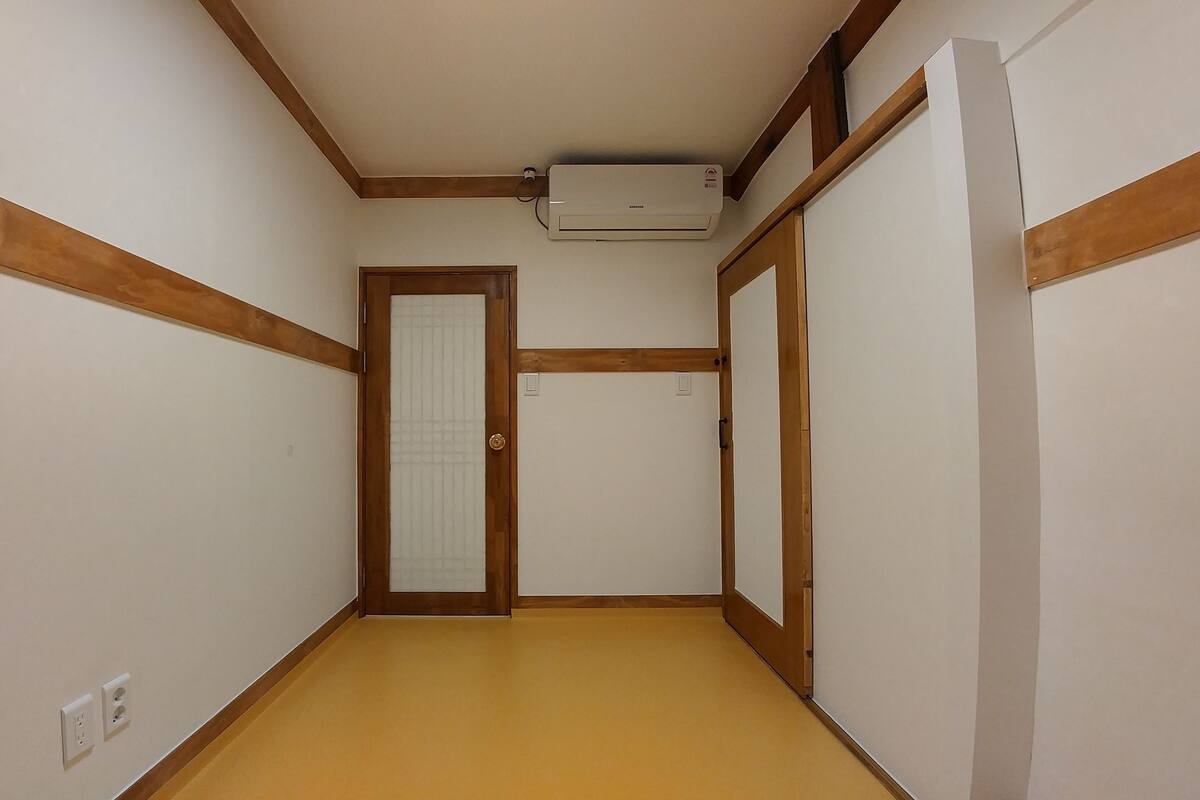 A narrow hallway with wooden trim, a door with a frosted glass panel, and an air conditioning unit mounted on the wall.