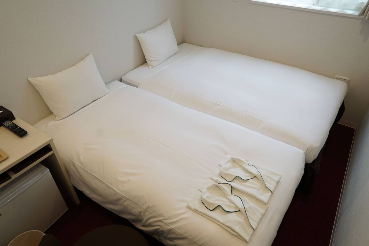 Hotellihuone, jossa on kaksi sänkyä, työpöytä ja pieni jääkaappi.