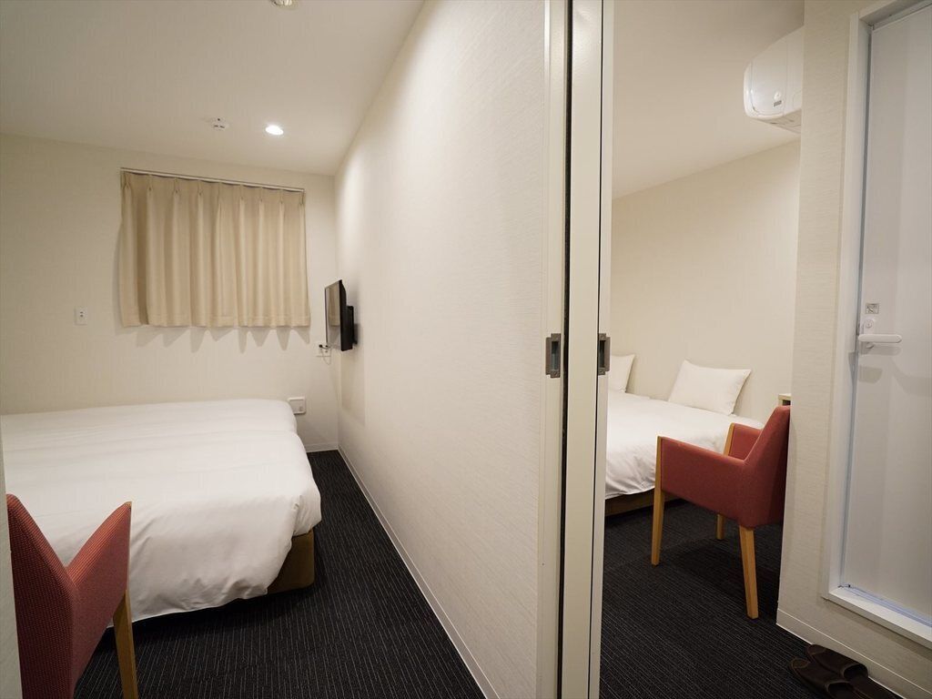 A hotel room with two beds, a red chair, a window, and a door.