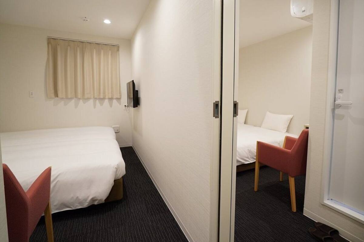 Hotellihuone, jossa on kaksi sänkyä, punainen tuoli, ikkuna ja ovi.