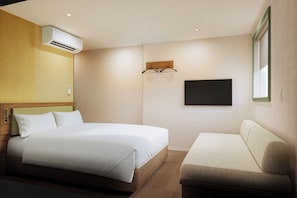 Une chambre d’hôtel comprenant un lit, un canapé, un appareil de climatisation, un téléviseur fixé au mur et une fenêtre.