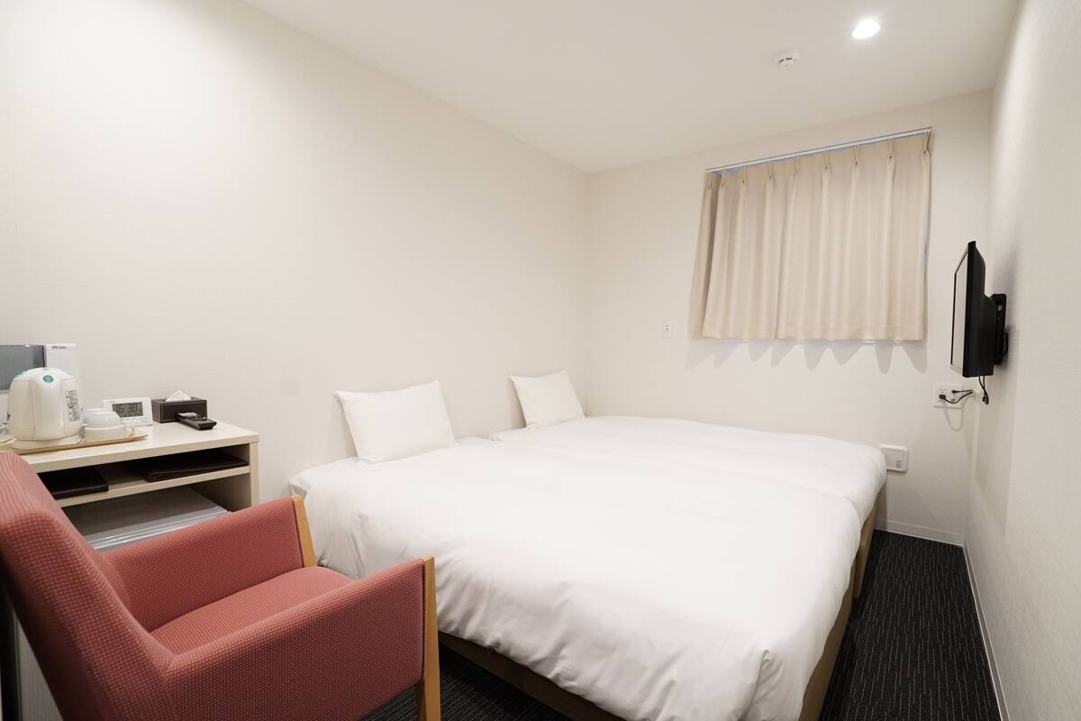 Hotellihuone, jossa on sänky, kirjoituspöytä, jossa on vedenkeitin, tuoli ja seinälle asennettu televisio.