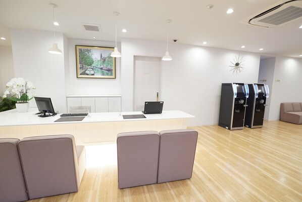 A reception area with a white counter, two computer monitors, a potted plant, and a clock on the wall.